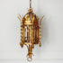 An ornate antique-style gold metal lantern pendant chandelier hanging against a white wall.