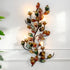 A decorative wall-mounted metal wall light with autumn holly leaf and vine flowers, in autumnal colours, lit with multiple warm candle-style bulbs against a white wall.