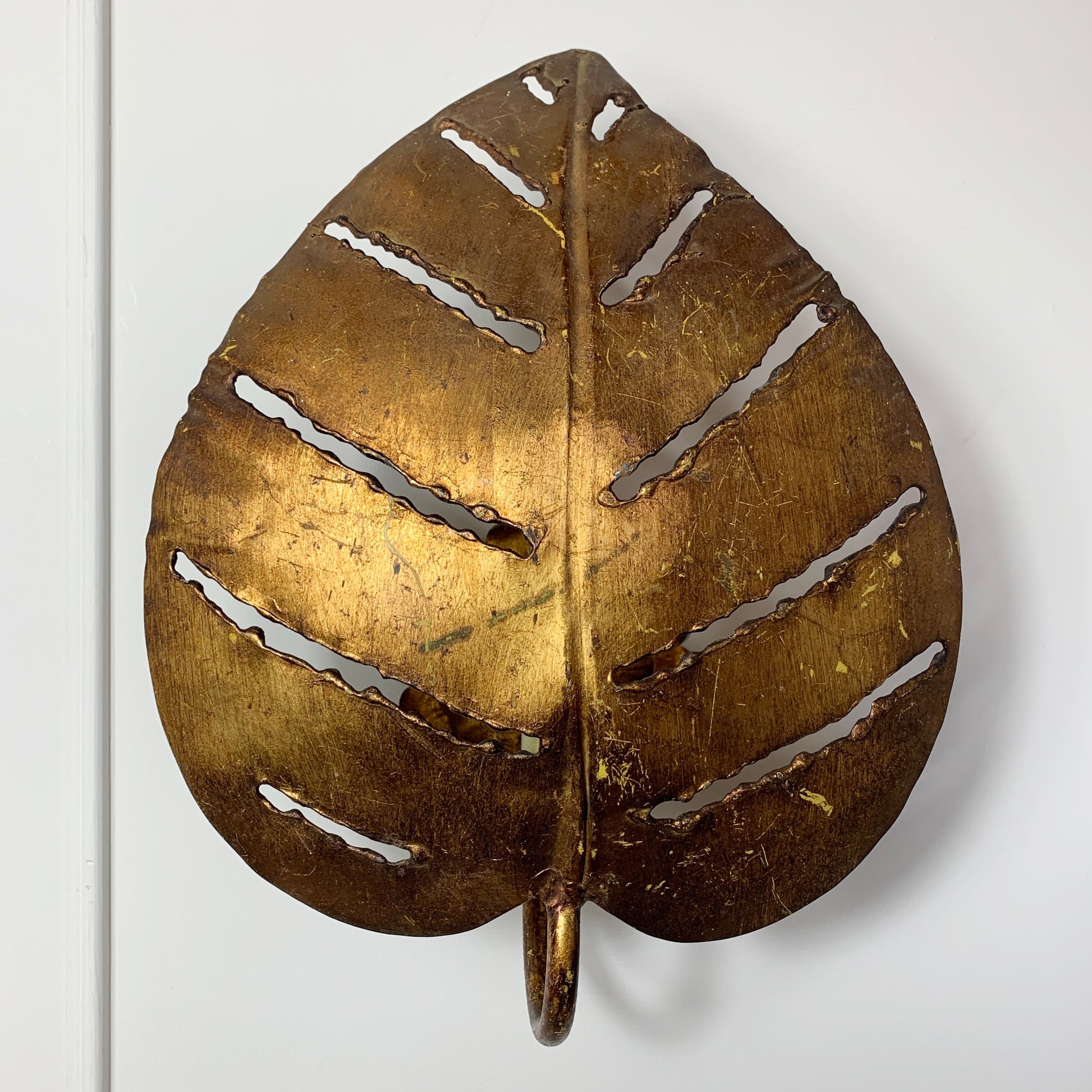 A decorative leaf-shaped designer wall light made of metallic gold-toned metal with cutout leaf veins, shown against a plain white background.