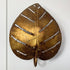 A decorative leaf-shaped designer wall light made of metallic gold-toned metal with cutout leaf veins, shown against a plain white background.