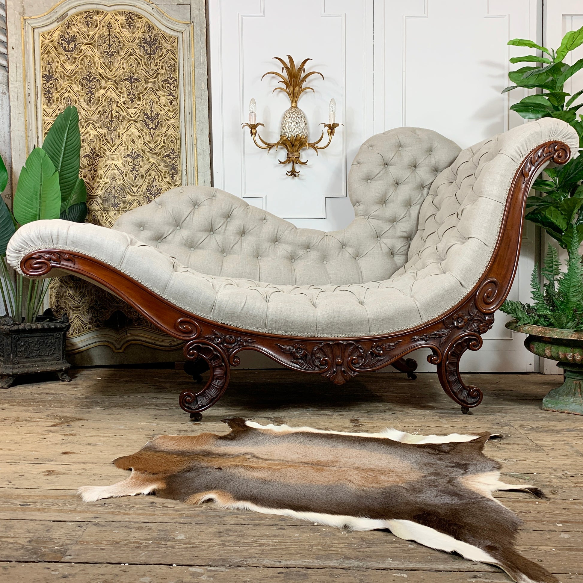 An elegant antique bittoned chaise lounge chair. Rococo Revival John Henry Belter Meridienne/Recamier with cream upholstery and carved dark wood legs, styled in a room with a cowhide rug on a wooden floor.