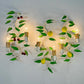 Three matching wall-mounted sconces with white vine and branch forms, green leaves, yellow lemon shapes, and small red berry accents, each holding a lit bulb against a plain light background.