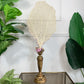 Antique large beige coral fan on a twisted gold-toned wooden stem, styled on a glass-topped table with green plants in the background.