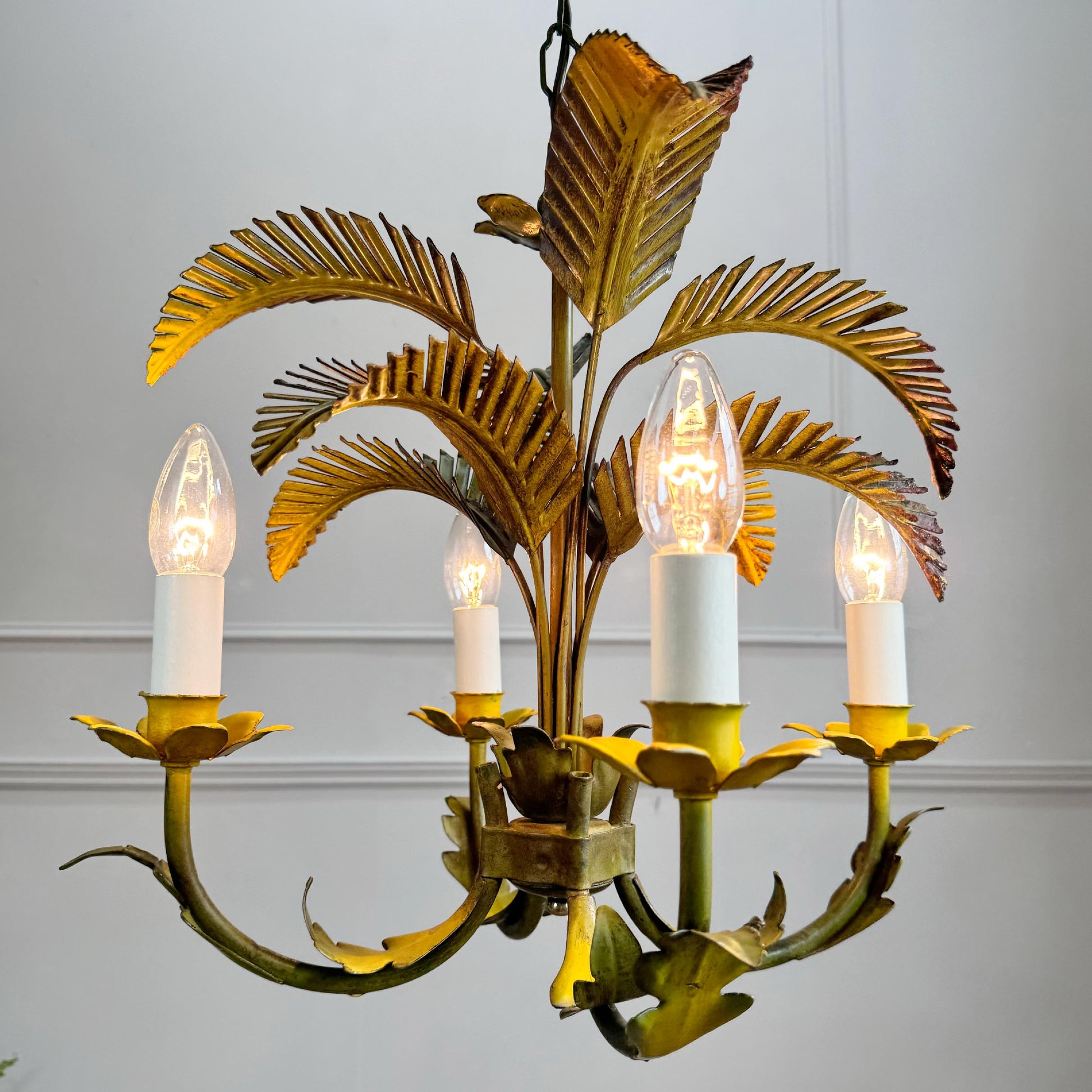 A vintage 1970s metal palm leaf chandelier with five candle-style bulbs, featuring a distressed gold and green metal finish with illuminated bulbs.