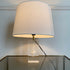 A Pierre Giraudon resin suspension desk lamp comprising a white shell held within a rectangular piece of resin or plexi-glass, and a brass finial, shown lit on a reflective glass table against a white wall.