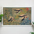 A framed vintage tapestry or wall hanging depicting three flying flamingos among detailed green, yellow, and red foliage, displayed on a white paneled wall with small green plants at the sides.