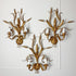 Three ornate Hans Kogl gold wall sconces with a wheat or reed-inspired leaf design, each holding two candle-style bulbs, mounted on a white paneled wall.