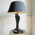 A tomasso barbi vintage table lamp featuring a sculpted black ceramic cobra snake base and a large black drum shade with a warm gold interior, displayed on a glass-topped side table against a cream wall.