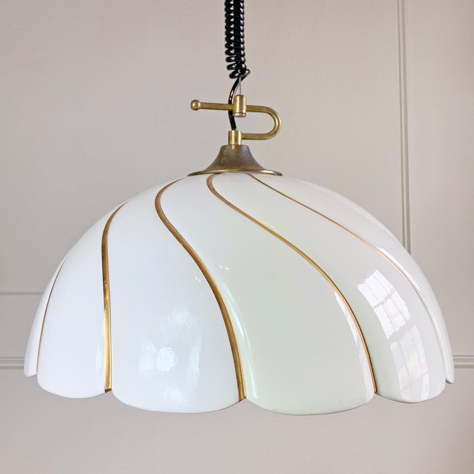 A vintage designer pendant light with a glossy white, petal-shaped shade accented by gold-toned metallic lines, suspended from a brass-colored ceiling mount with a black coiled cord.