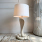 A Tommaso Barbi table lamp shaped like a coiled cobra snake in an off-white ceramic, with a matching off-white drum shade, set on a rustic wooden floor against a white paneled wall.