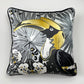 A square decorative silk pillow featuring a stylized toucan illustration in black, white, gray, and gold, with a black piped edge, shown against a light gray background.