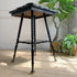 A black ebonised wooden corner table with turned legs and brass-toned claw casters, photographed in a styled interior setting with potted plants and a light wall background.
