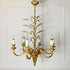 A decorative six-light wall or ceiling chandelier with an ornate gold metal frame styled like a wheatsheaf, featuring candle-style bulbs on curved arms against a white paneled wall.