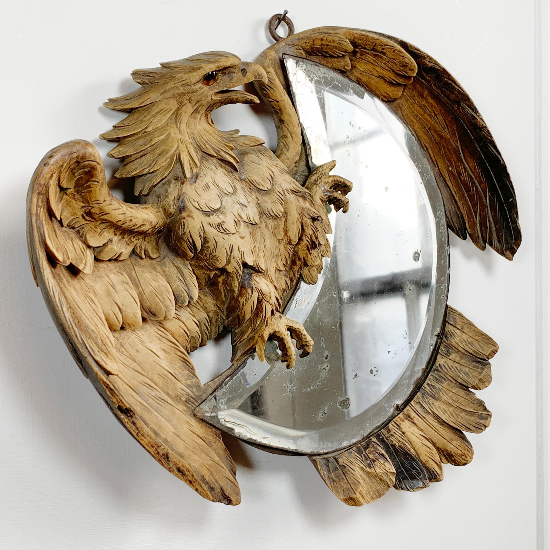 A carved vintage wooden wall mirror featuring an eagle with spread wings and a crescent mirror.
