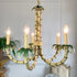 A decorative chandelier shaped like a bamboo stalk and branches, with five candle-style lights turned on, set against a white paneled wall.