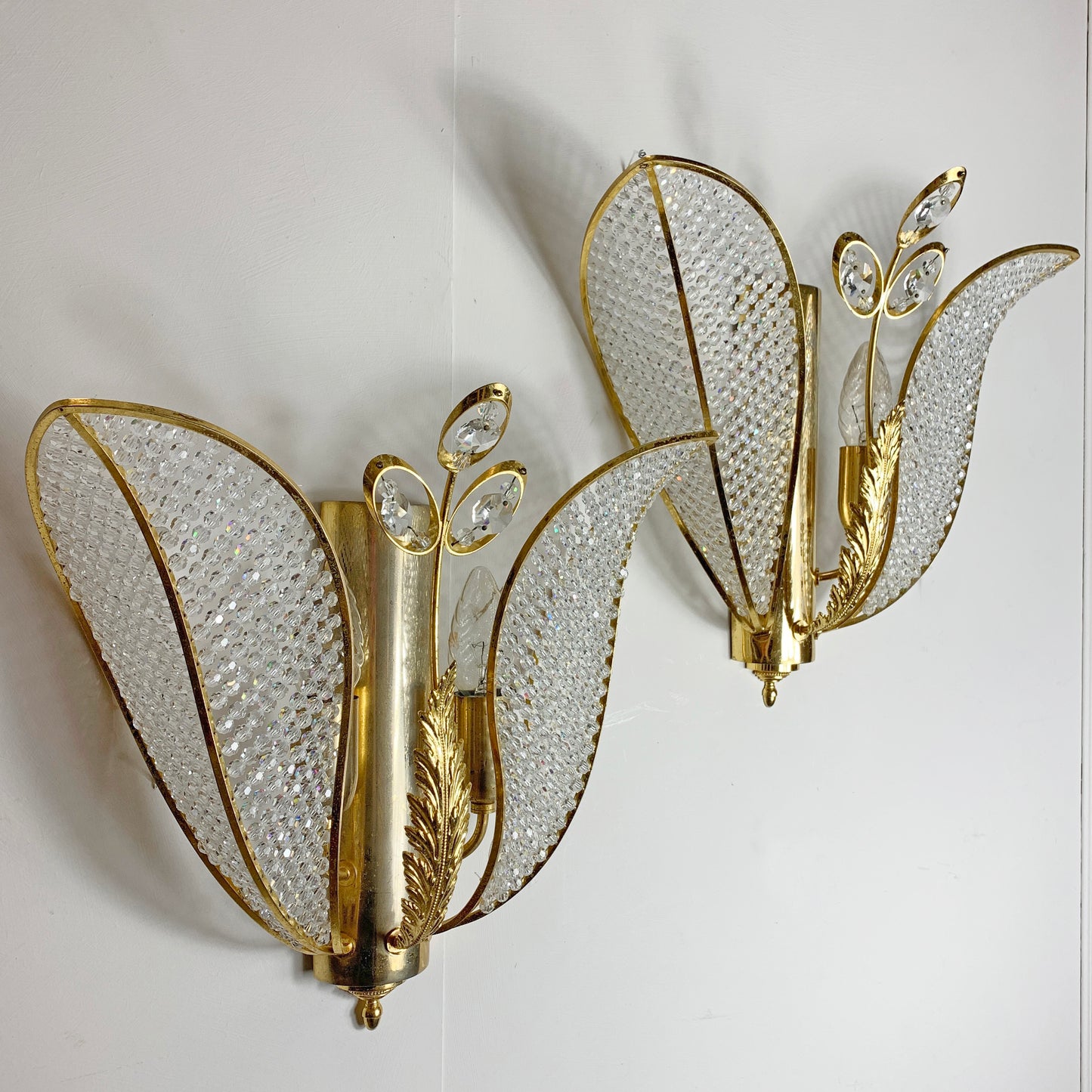 A pair of vintage gold butterfly wall sconces with textured clear crystal wings, mounted on a plain white wall.
