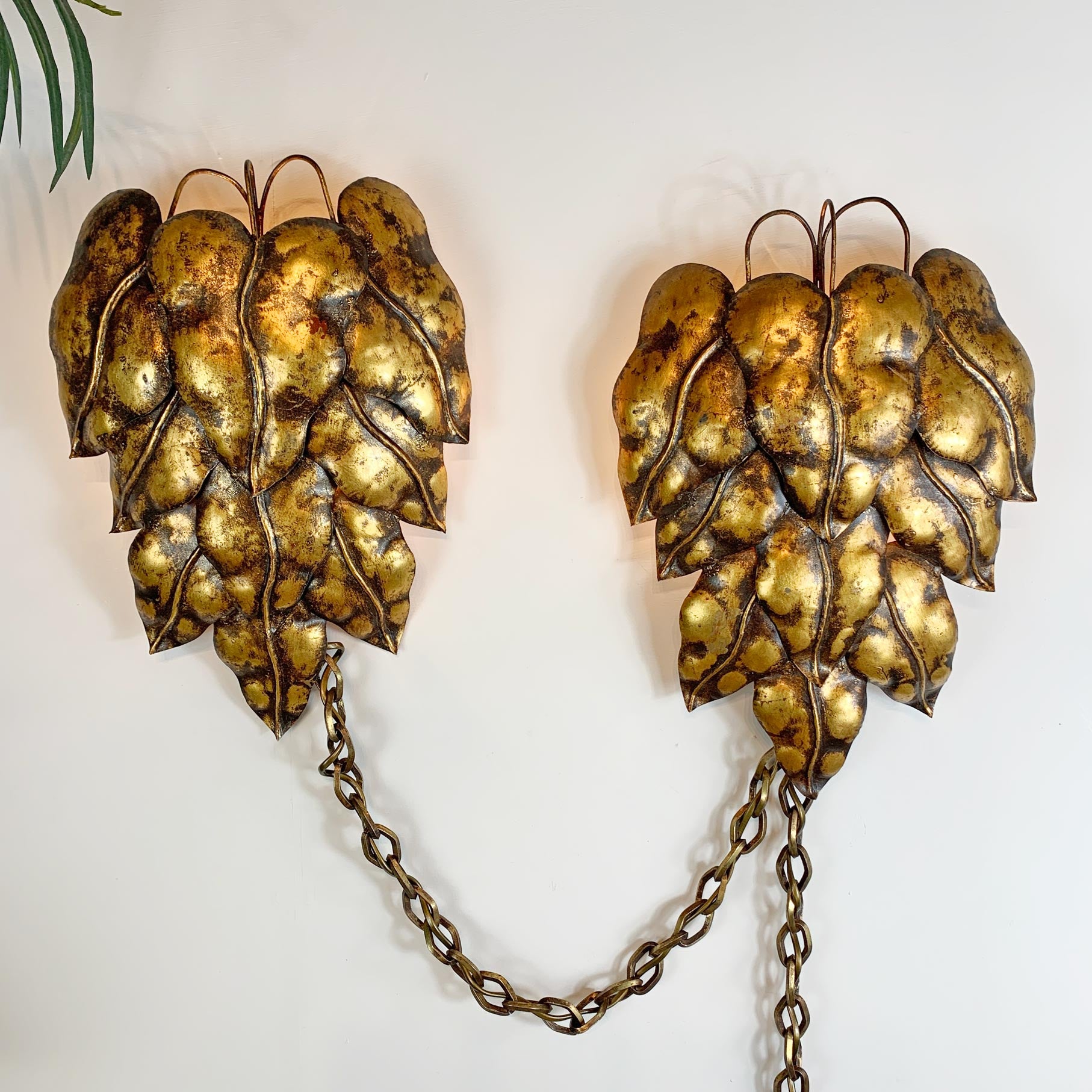 A pair of vintage metallic swag wall sconces shaped like textured gold and bronze pinecones, connected by a short chain, mounted on a plain white wall.