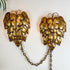 A pair of vintage metallic swag wall sconces shaped like textured gold and bronze pinecones, connected by a short chain, mounted on a plain white wall.