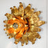 A decorative wall-mounted light fixture shaped like a sunflower, with metallic gold and orange petals surrounding a clear bulb socket.