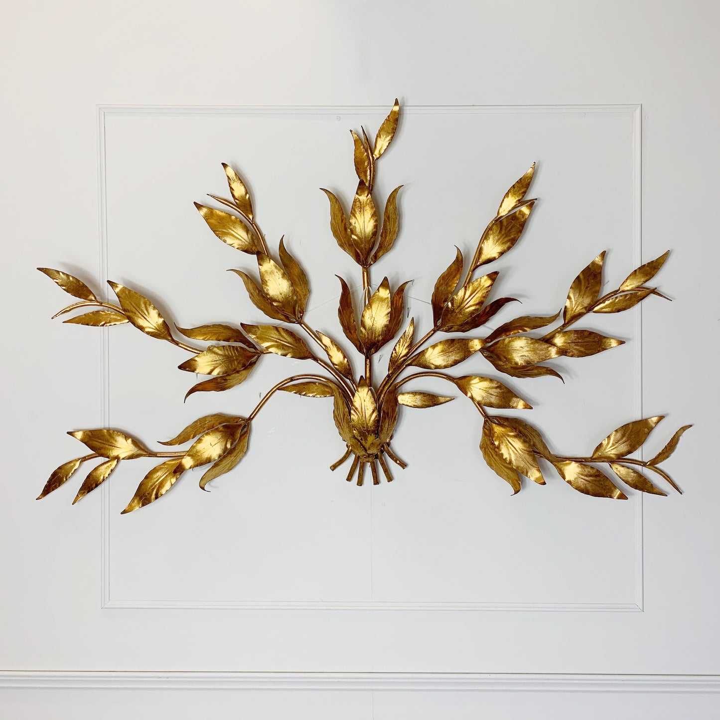 A decorative hans kogl gold leaf wall light in a leafy branch motif, mounted on a white paneled wall.
