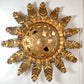 A decorative vintage sunburst wall sconce with a textured gold finish, featuring a central circular cutout medallion and radiating sculpted rays, shown against a plain white wall.