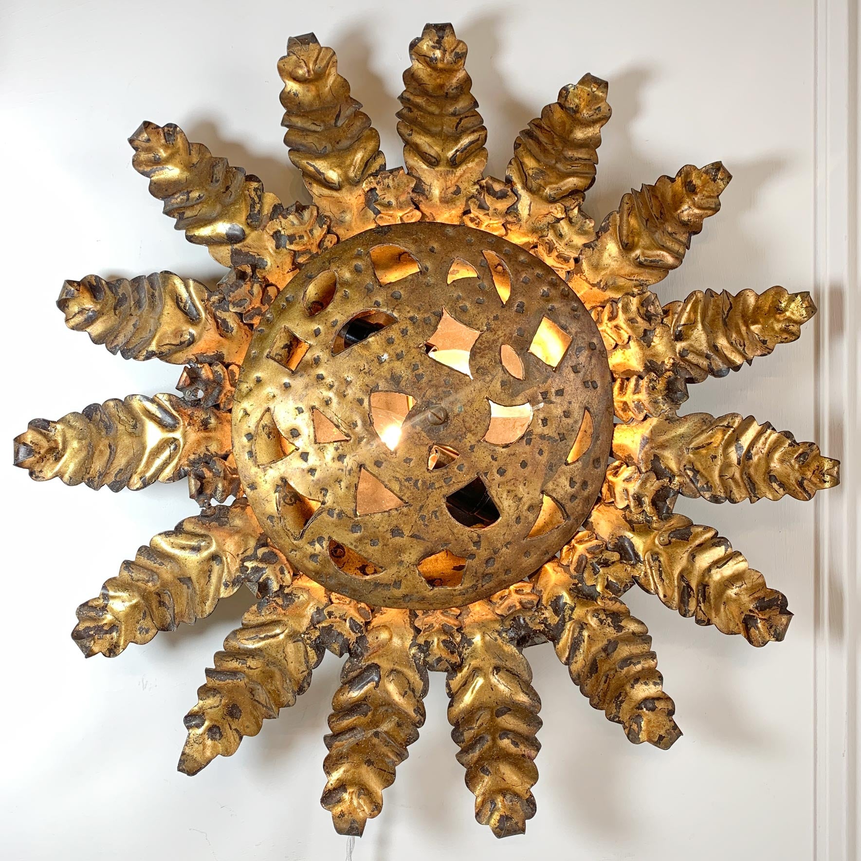 A decorative vintage sunburst wall sconce with a textured gold finish, featuring a central circular cutout medallion and radiating sculpted rays, shown against a plain white wall.