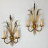 A pair of vintage bulrush wall sconces with gold-toned metal frames, candle-shaped bulbs, and black decorative accents, mounted on a plain white wall.