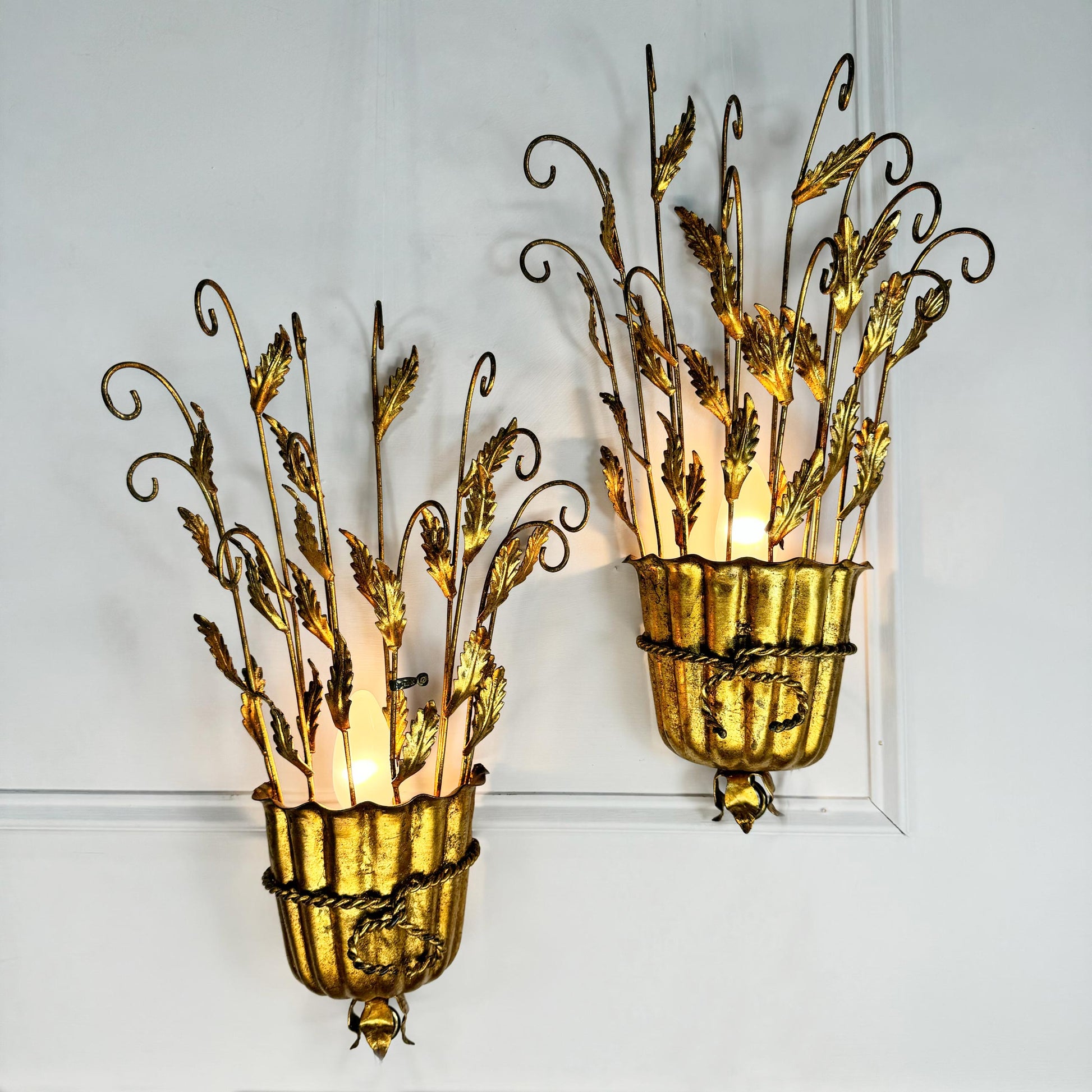 A pair of ornate gold and bronze vintage Italian metal wall sconces with leafy vine designs, mounted on a white paneled wall.