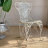 Antique regency white wrought iron garden chair with a woven seat and backrest, styled on a beige woven rug next to a potted green plant.
