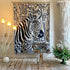 A large woven tapestry featuring a detailed black and white zebra illustration with beige and gray botanical elements, hanging on a gold rod in a styled room with decorative plants, a gold side table, and warm wall lighting.