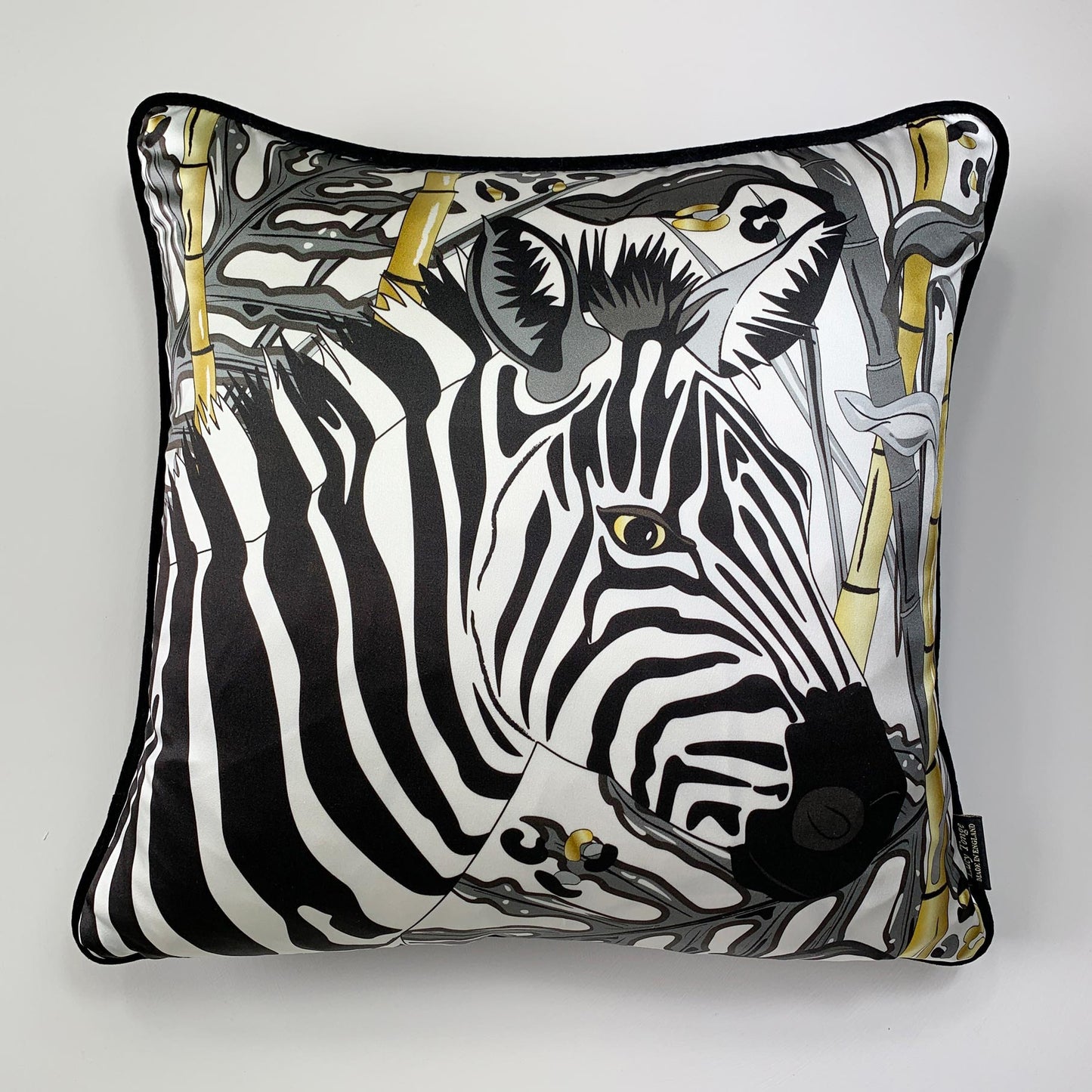 Square decorative silk pillow featuring a stylized black and white zebra print with gold accents, finished with a black piped edge, shown against a plain light gray background.