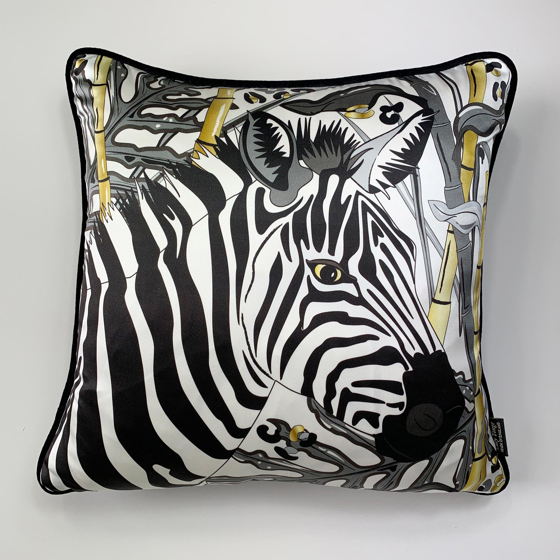 Square decorative silk pillow featuring a stylized black and white zebra print with gold accents, finished with a black piped edge, shown against a plain light gray background.